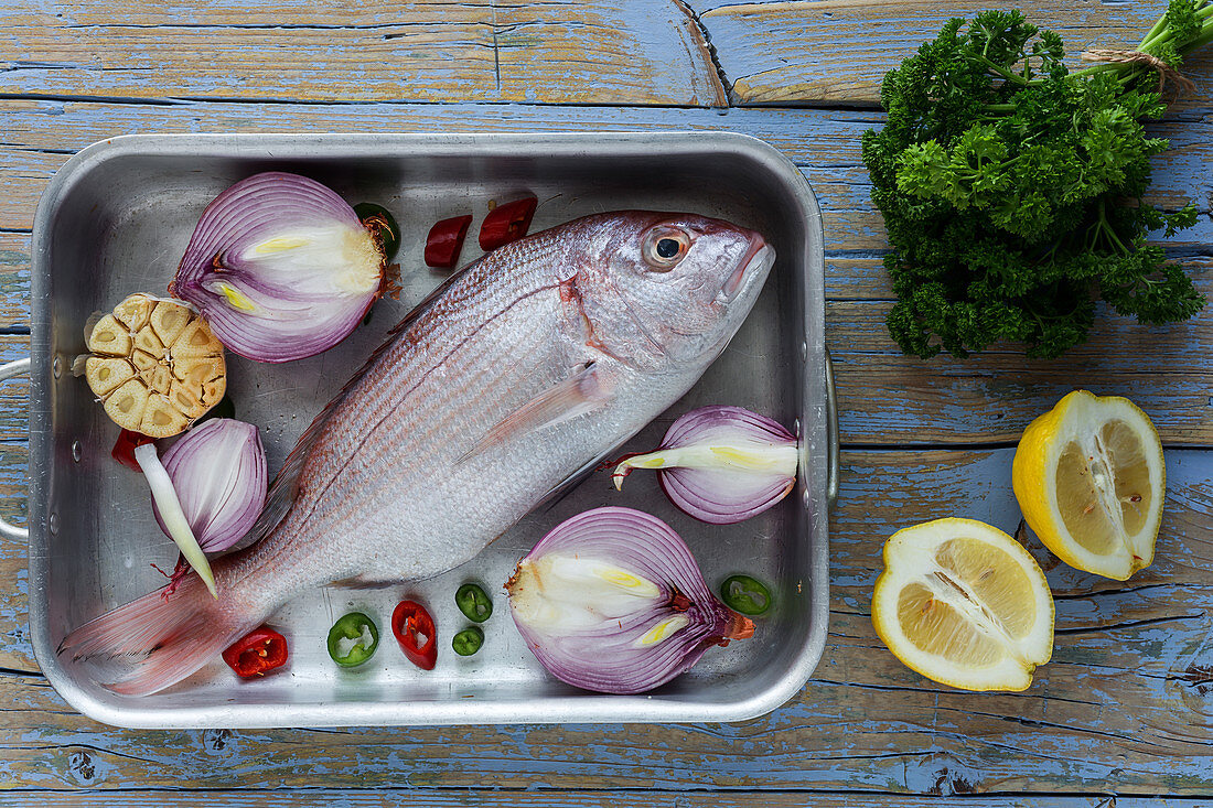 Fresh vegetables and raw fish lying in metal baking pan on lumber tabletop