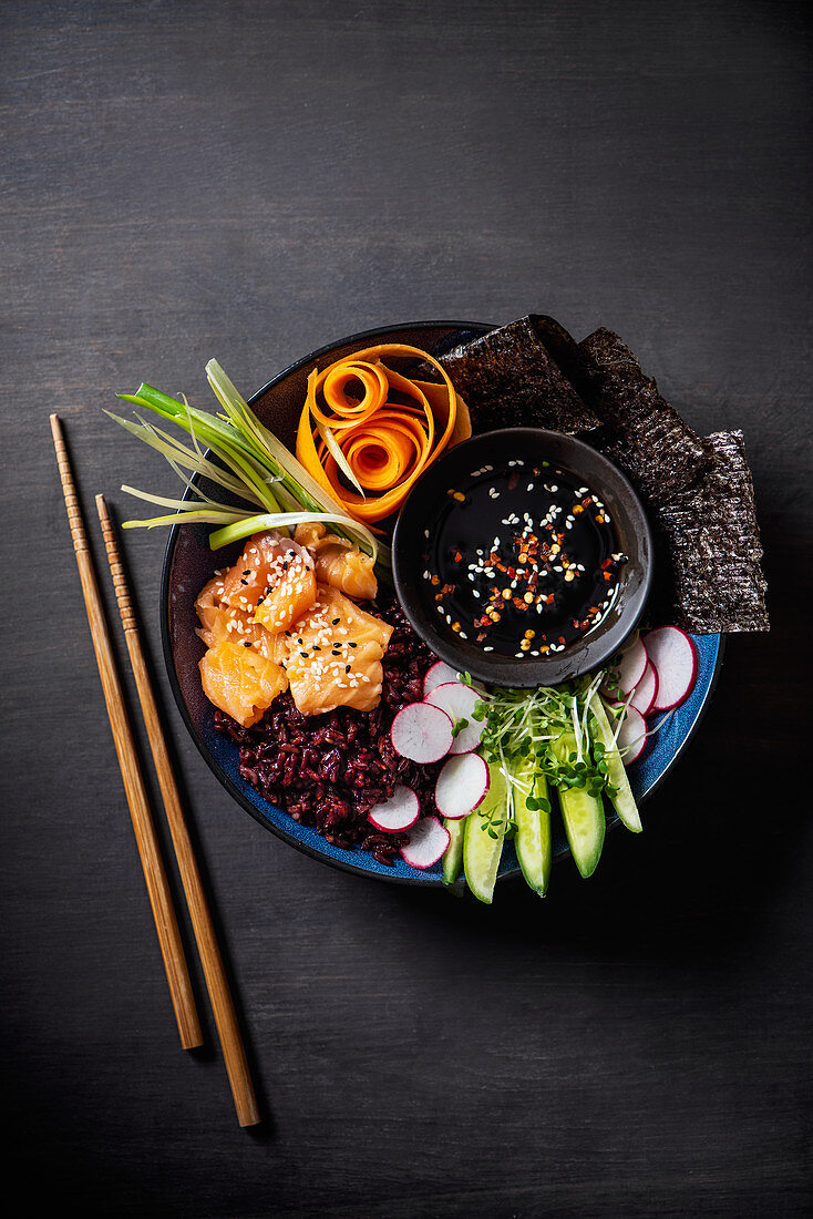 Sushi Buddha Bowl mit rotem Reis, Lachs, Nori, Gemüse und Sojasauce (Asien)