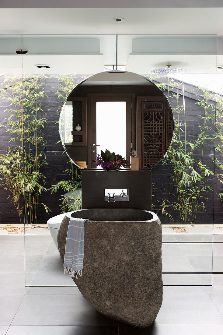 Basalt washbasin and wall mirror in front of glass wall