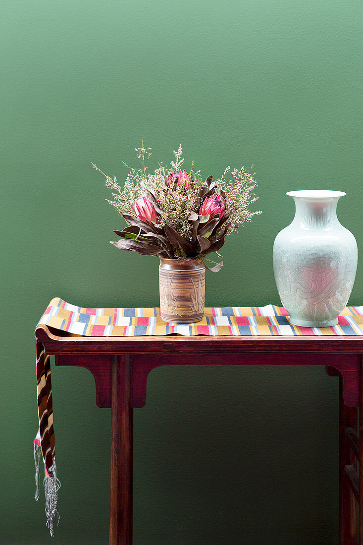 Console with table runner, vase and bouquet of flowers in front of green wall