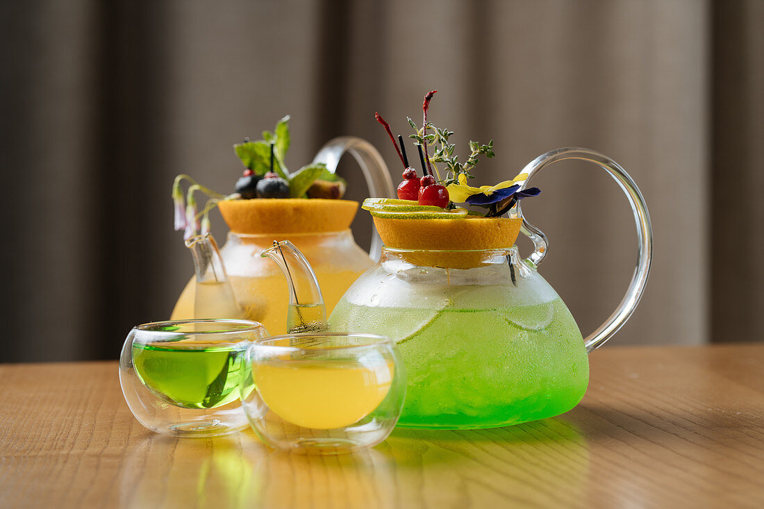 Green and yellow cocktails served in glass jugs and cups