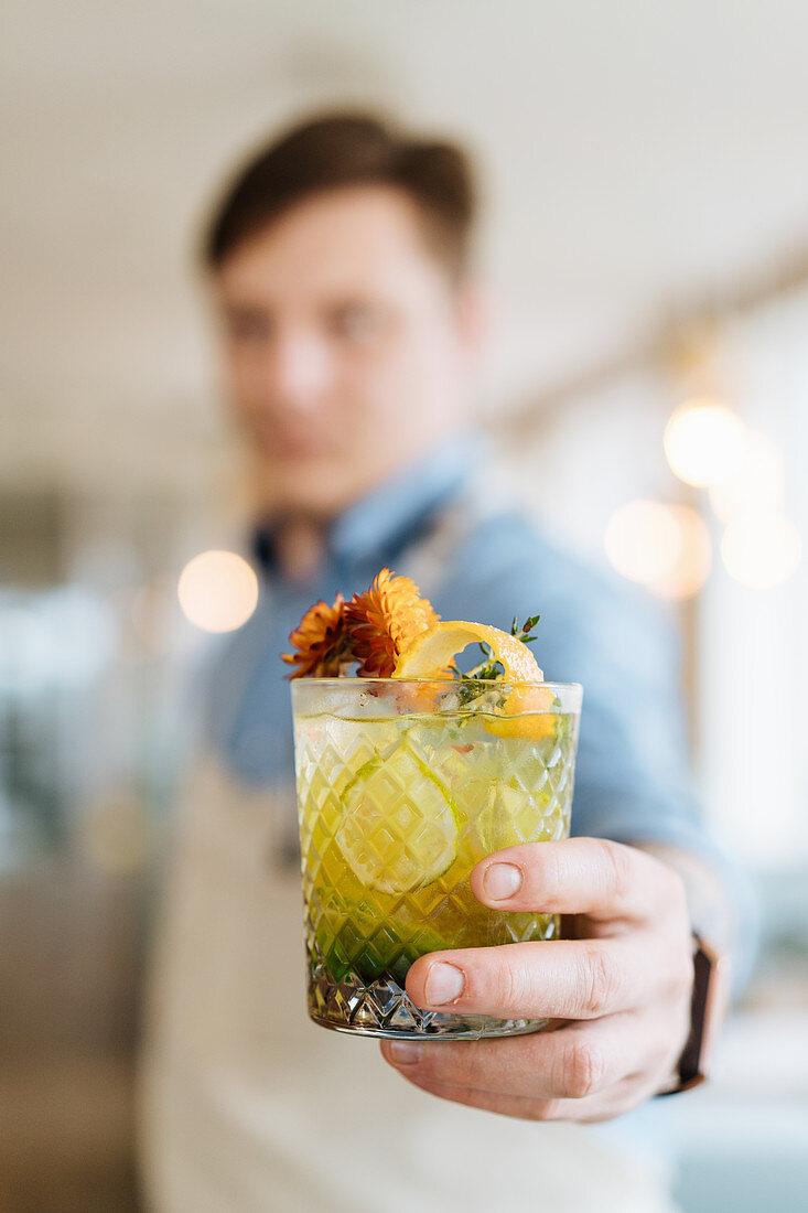 Barkeeper serviert Cocktail garniert mit Blüten und Orangenschale