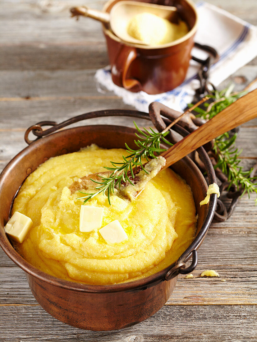 Cooked polenta in a copper kettle with pieces of butter and rosemary