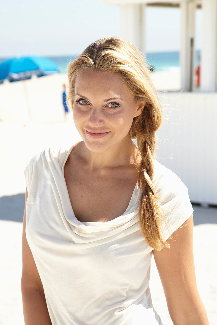 A blonde woman on a beach wearing a beige summer dress