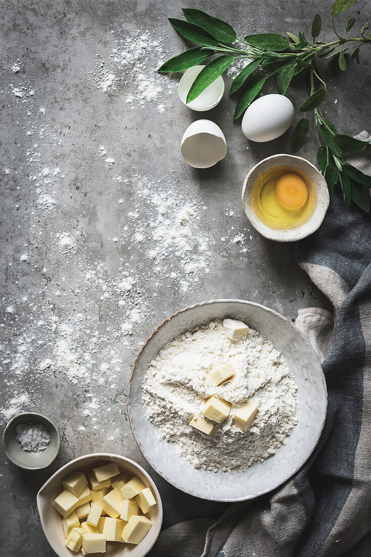 Flat lay of beautiful arrangement with bowl of flour and butter with eggs on marble table with green branch