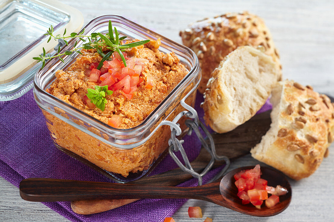 Tofu and tomato spread in a glass jar served with bread rolls