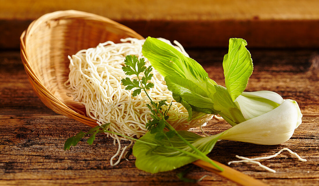 Stillleben mit Pak Choi, Mie-Nudeln im Flechtsieb und Koriander (Asien)