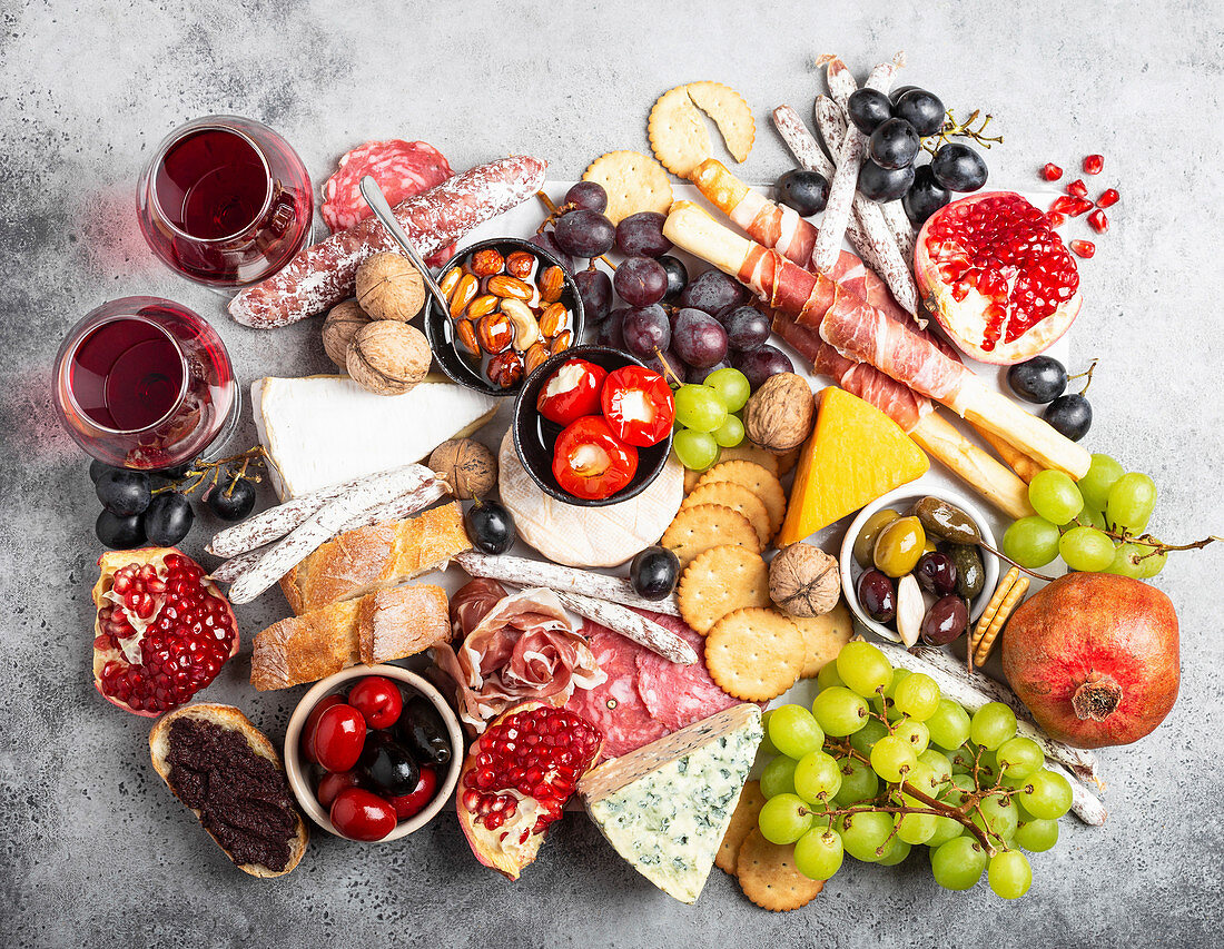 Reichhaltige Antipastiplatte aus Snacks und Vorspeisen, Käse, Fleisch, Oliven, Brot, Obst, Canapés und Rotwein