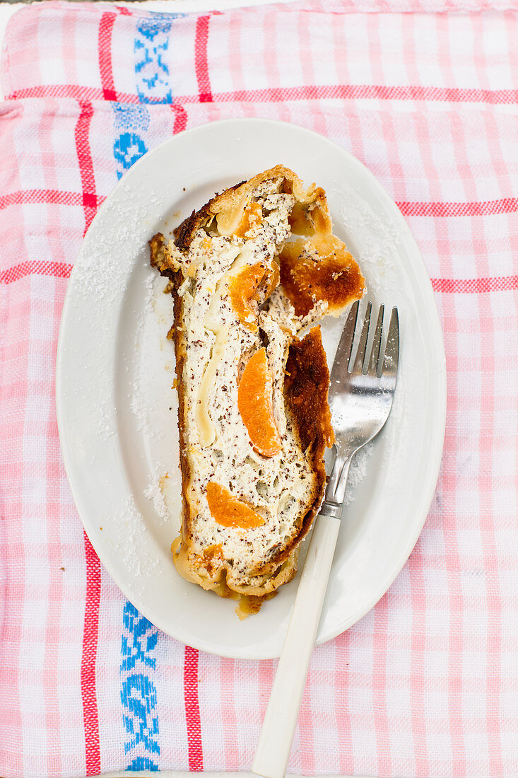 A piece of curd strudel with apricots and poppy seeds on a plate