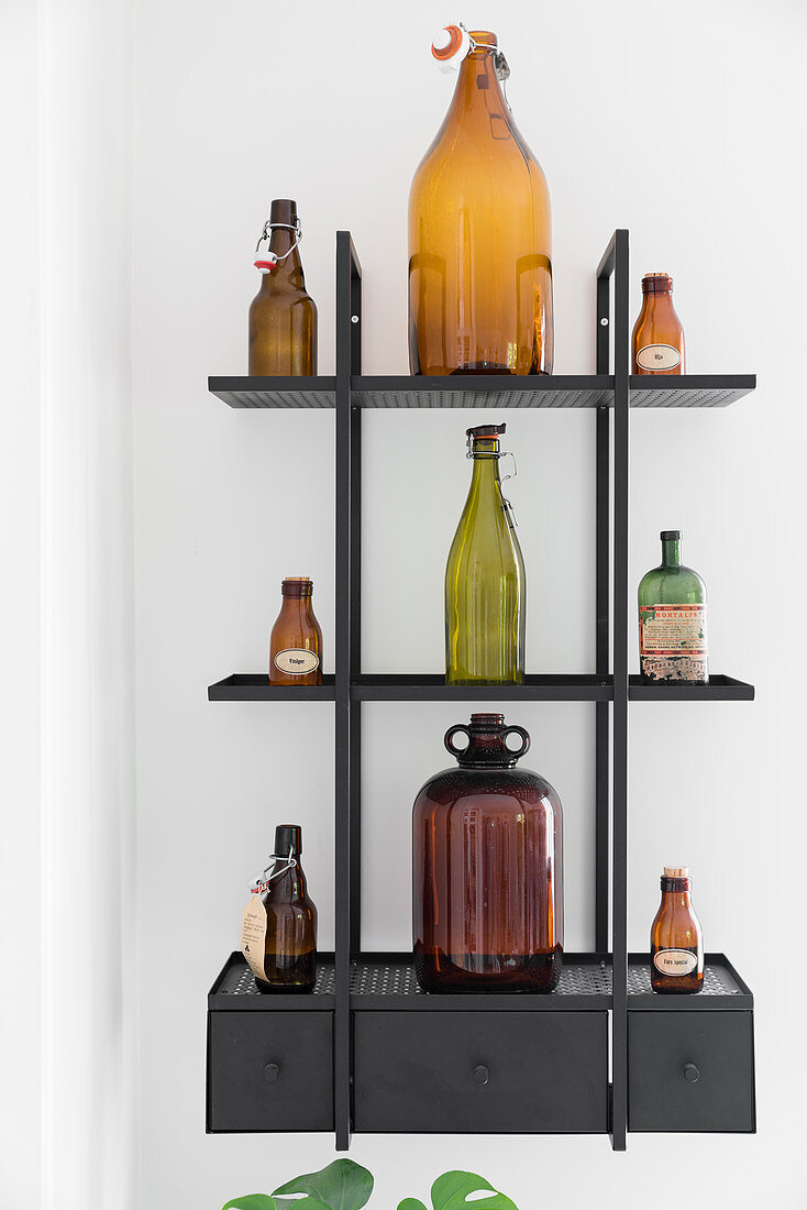 Old glass bottles on black wall-mounted shelves with drawers