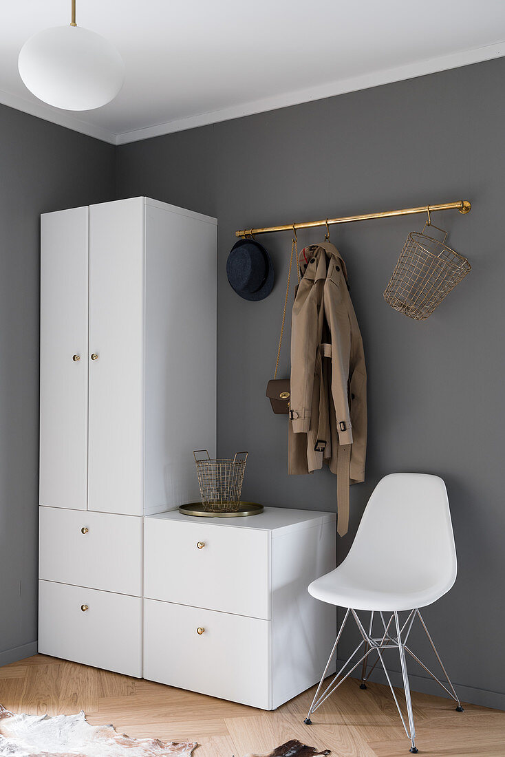 White wardrobe and classic chair below coat rack on grey wall