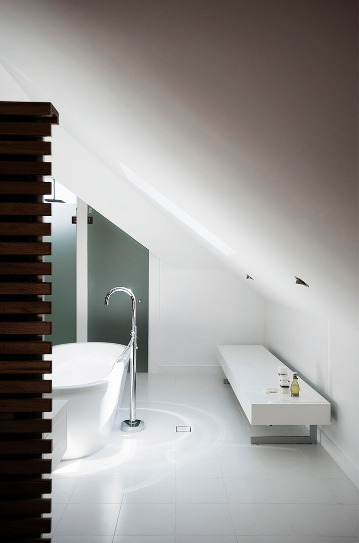 Freistehende Badewanne mit Standarmatur und Bank in weißem Designerbad mit Dachschräge