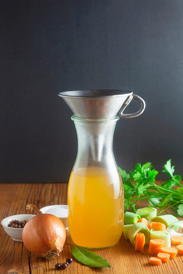 Homemade vegetable stock with a funnel in a glass carafe