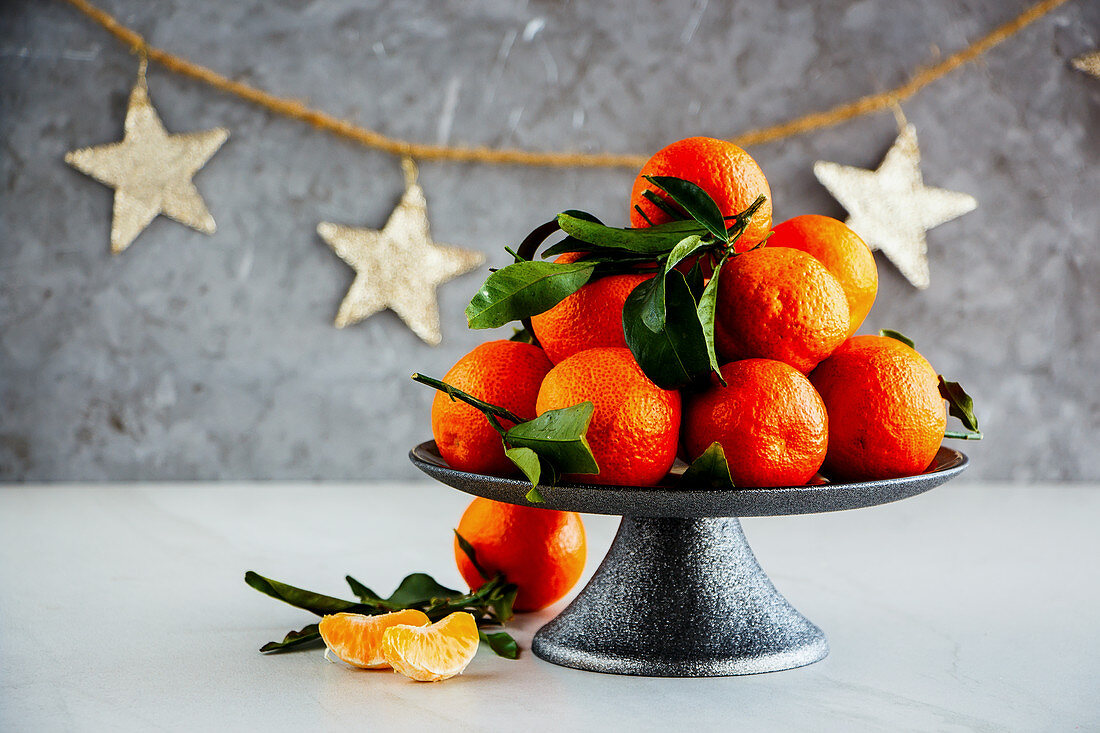 Mandarinen mit Blättern auf Servierständer, im Hintergrund Weihnachtsdekoration