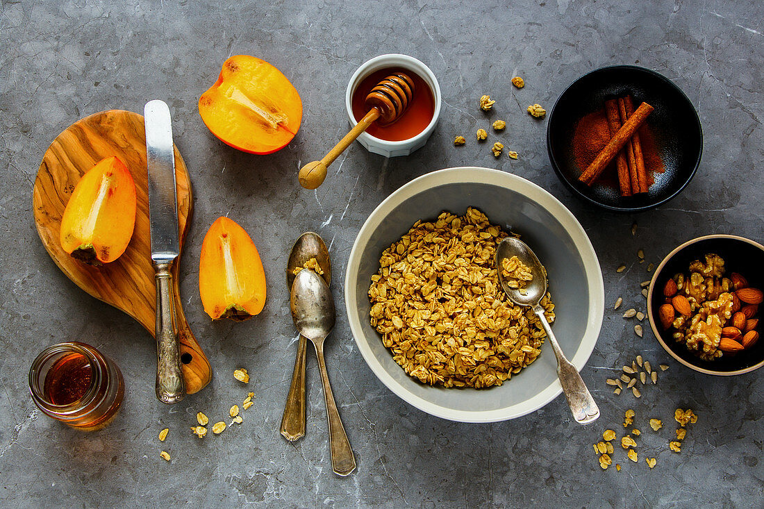 Healthy breakfast variety of cinnamon granola, fresh persimmon, maple syrup, honey and nuts