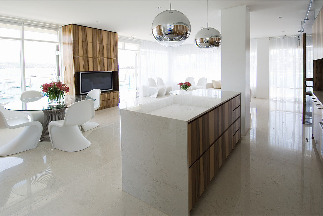 Kücheninsel aus Marmor, weiße Designerstühle um Glastisch und Fernsehregal in offenem Wohraum