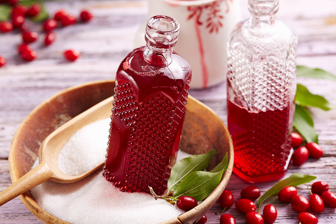 Bottles of homemade cornelian cherry syrup in a wooden bowl with sugar