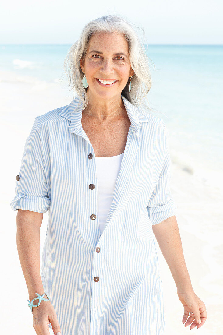 A mature woman with white hair on a beach wearing a striped blouse and a top