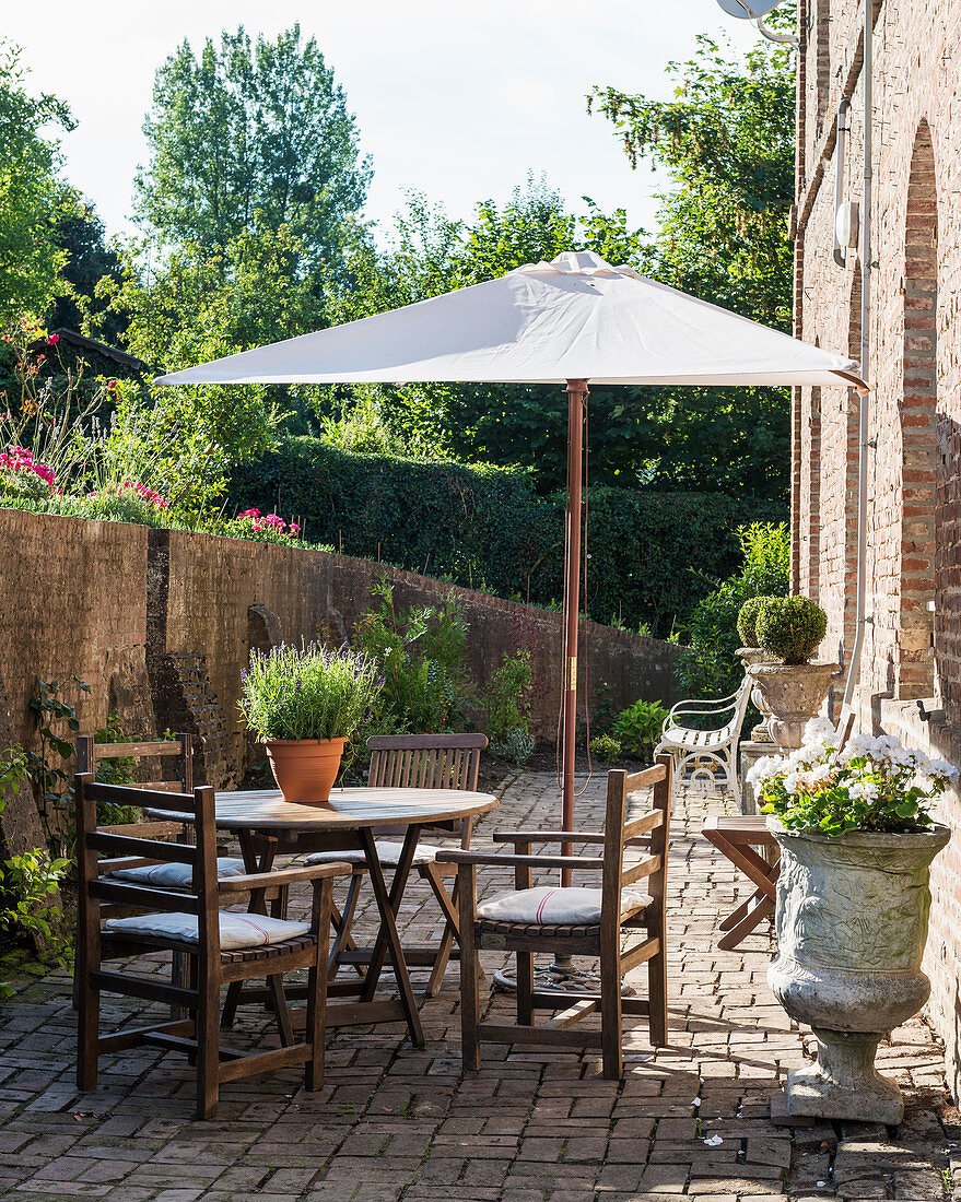 Teakholzmöbel, Steinurnen und Sonnenschirm auf sonniger, gemauerter Terrasse