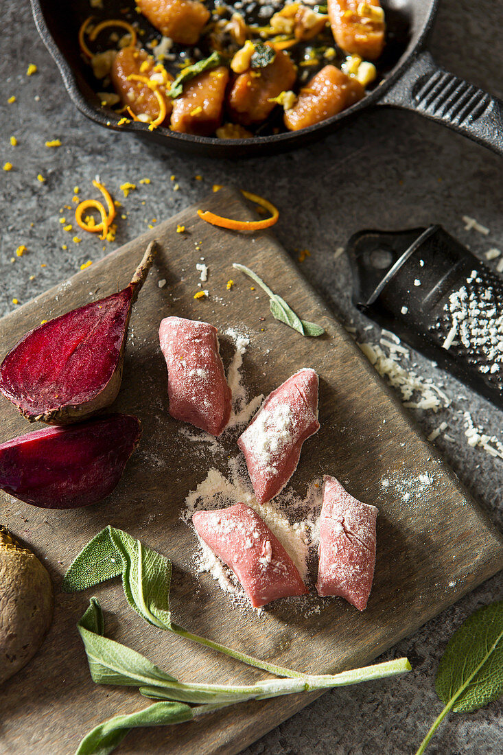 Beetroot gnocchi on a chopping board with fresh sage, raw beetroot, parmesan and cooked dish