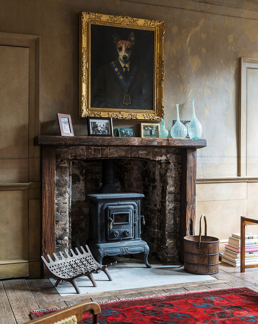 Gilt-framed, whimsical dog portrait above old log-burning stove in antique fireplace