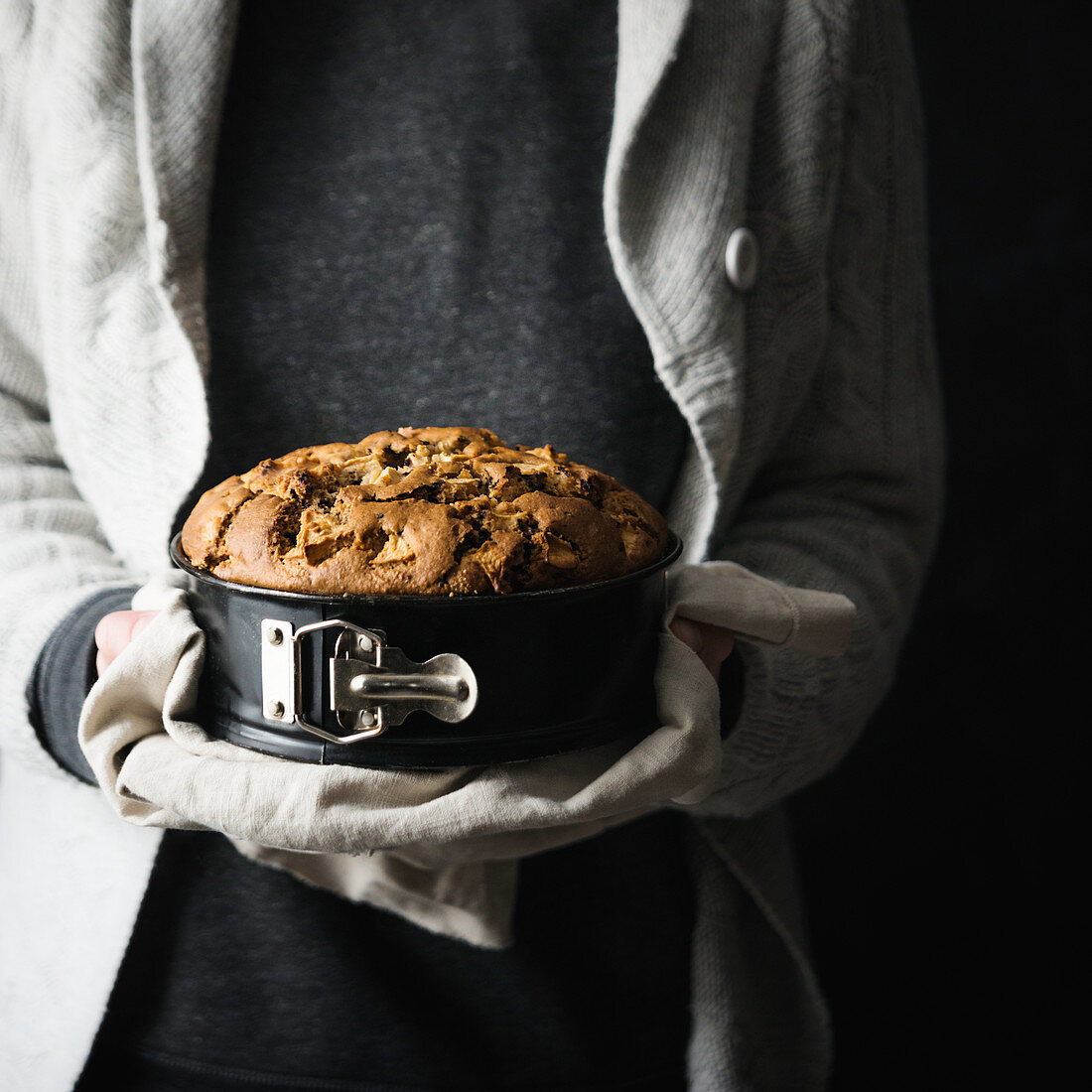 A woman holding a vegan apple cake in a springform pan