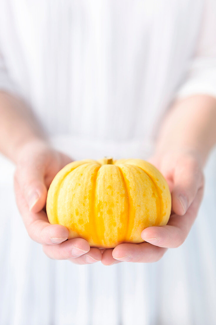 A woman holding a yellow pumpkin in both hands