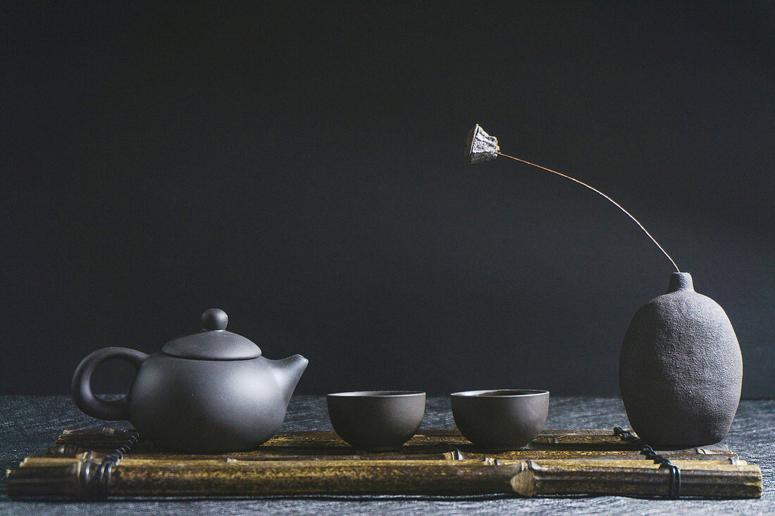 A dark grey tea pot with two tea bowls against a dark background