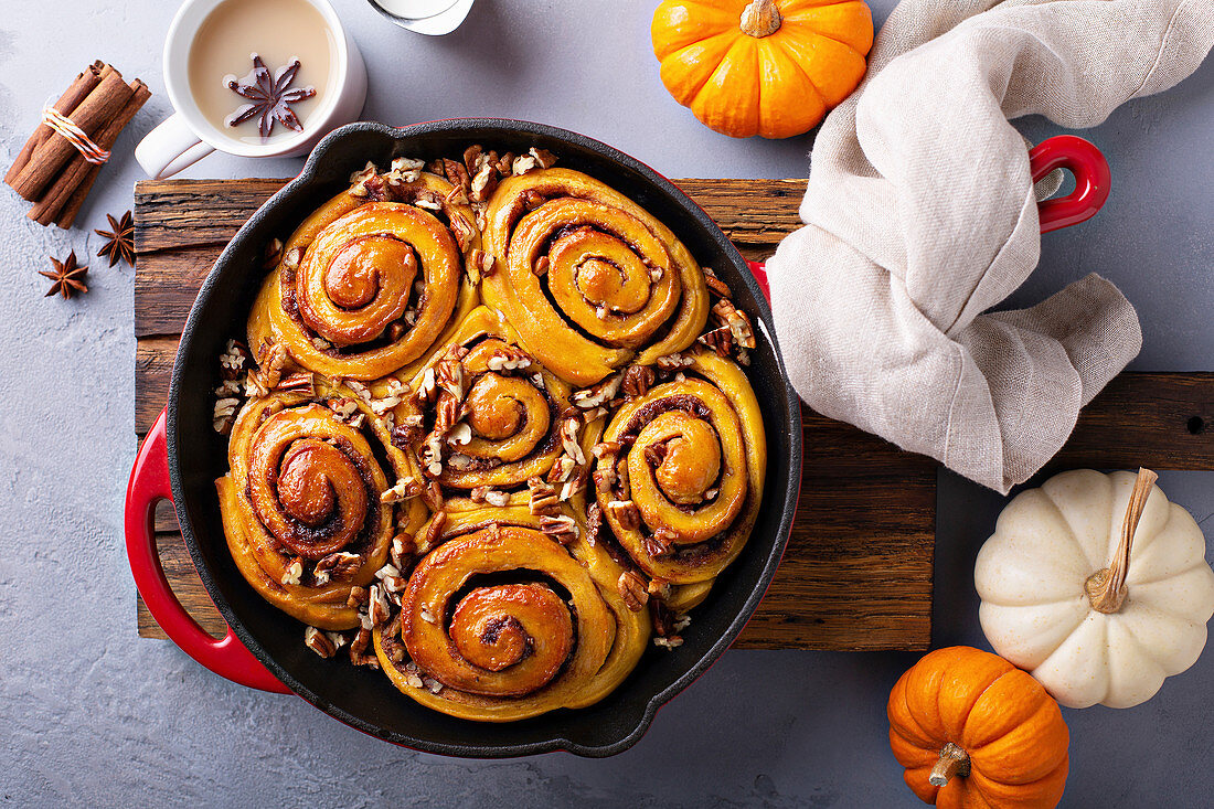 Pumpkin cinnamon rolls in a cast iron pan with nuts and sugar glaze