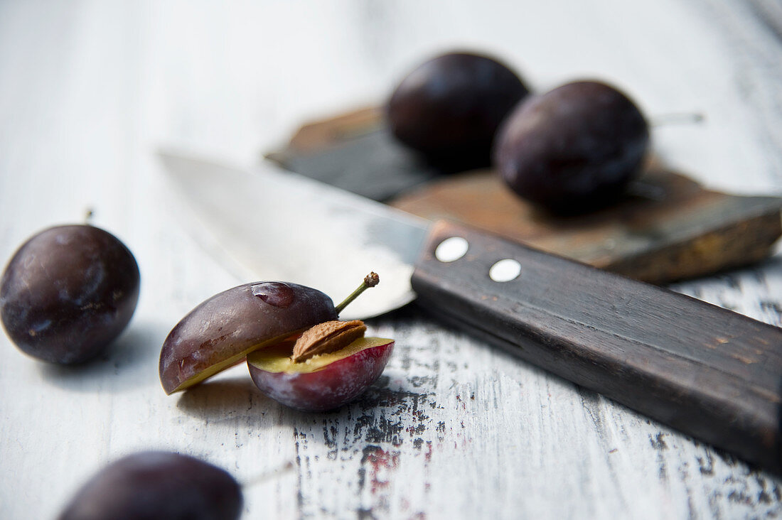 Damsons halved and whole with a knife on a rustic wooden surface