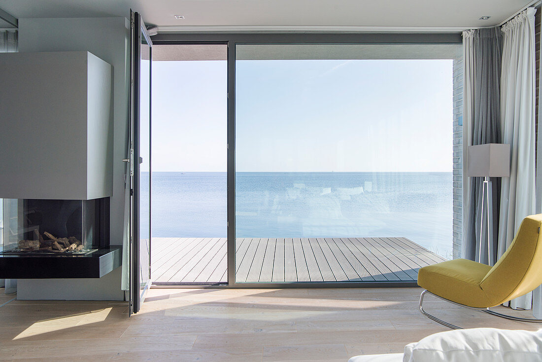 Uninterrupted sea view through floor-to-ceiling windows and across wooden deck without balustrade