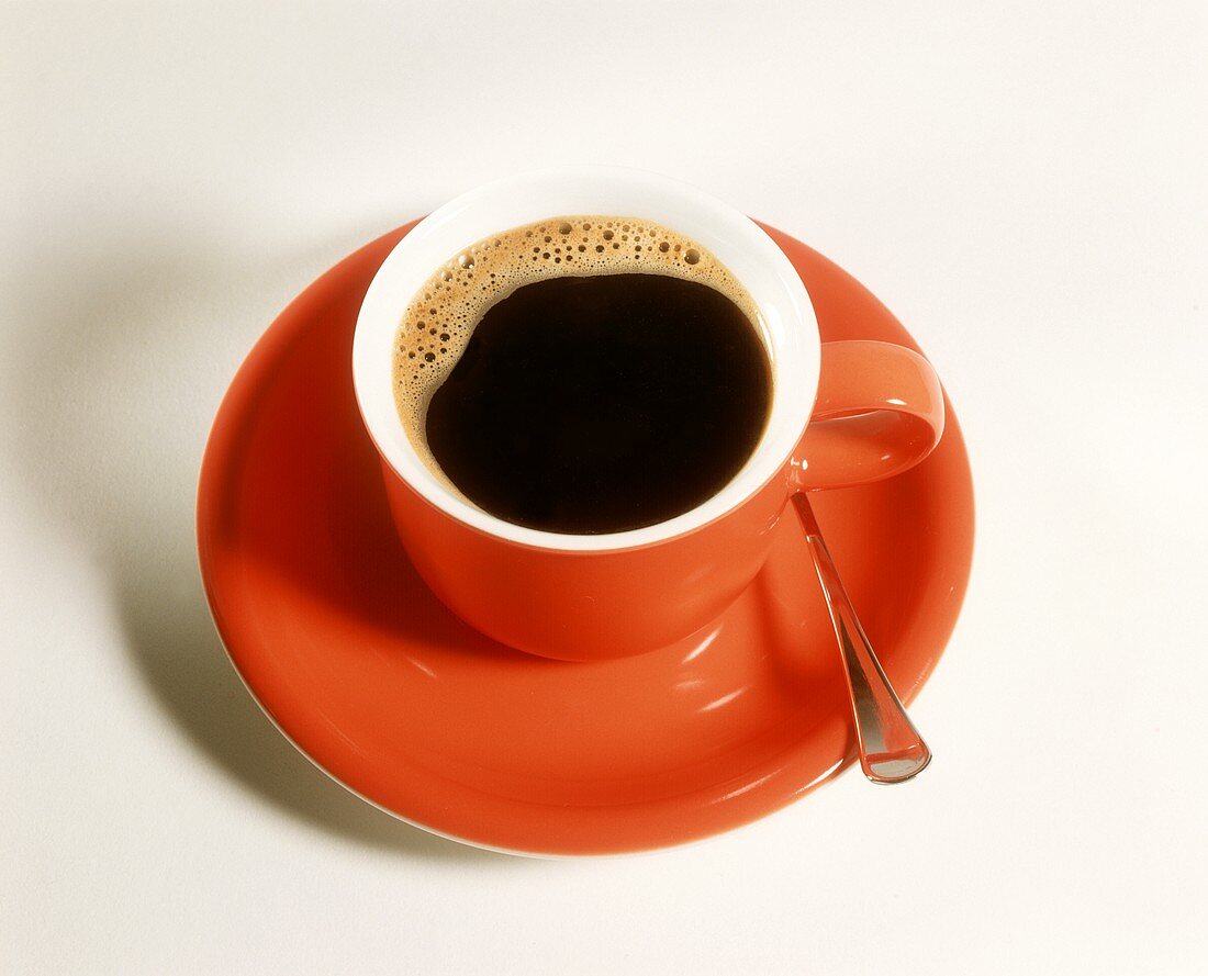 Eine rote Tasse mit schwarzem Kaffee & Kaffeelöffel