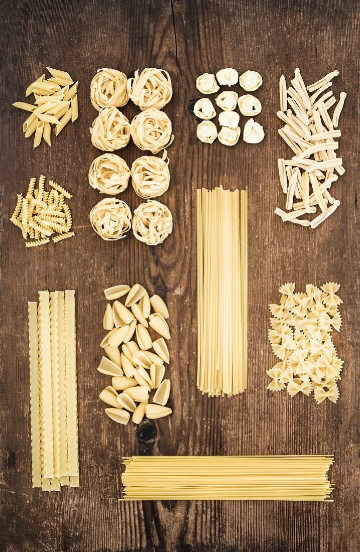 Different types of Italian uncooked pasta on rustic wooden table background