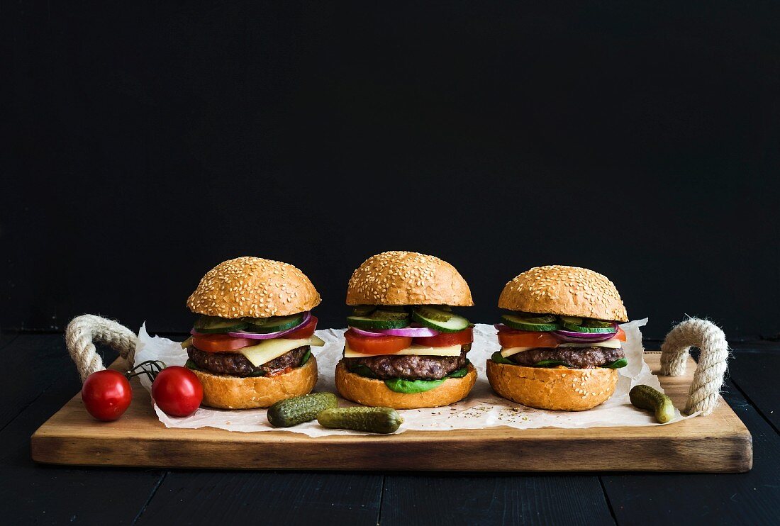 Fresh homemade burgers on wooden serving board over black background