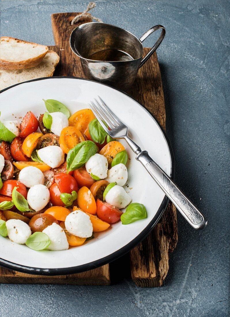 Italian Caprese salad with cherry tomatoes, small mozzarella and fresh basil in white enamel plate