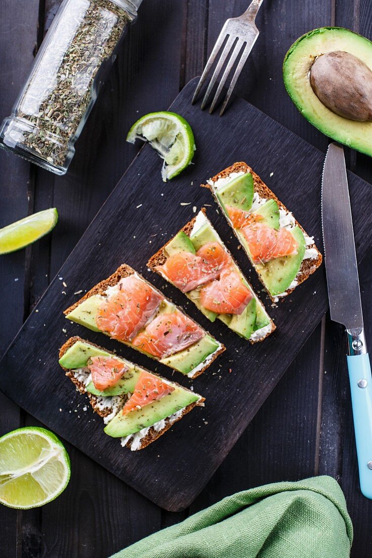 Sandwich mit Frischkäse, Avocado und geräuchertem Lachs auf schwarzem Holzbrett