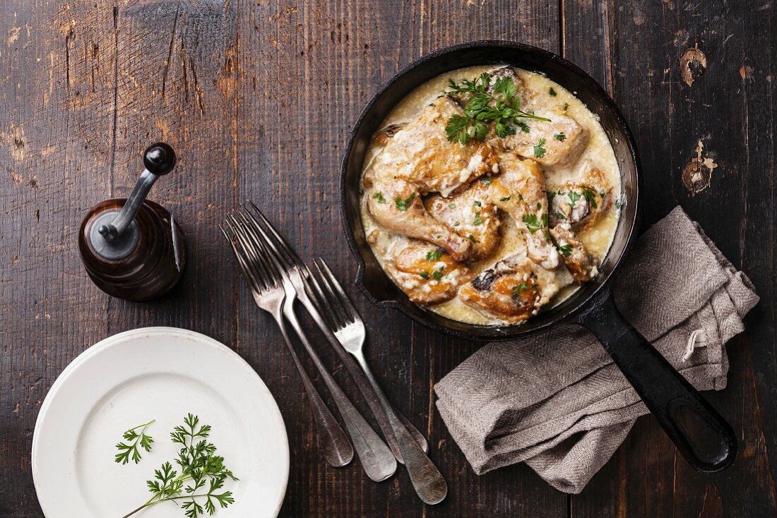 Roasted chicken with creamy garlic sauce in cast iron frying pan on dark wooden background