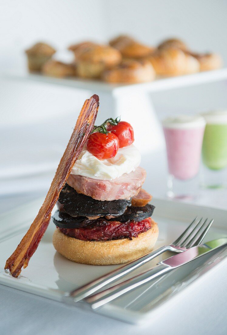 English Muffin mit Schinken, Pilzen, Tomaten und Speck, im Hintergrund Smoothies und Gebäck