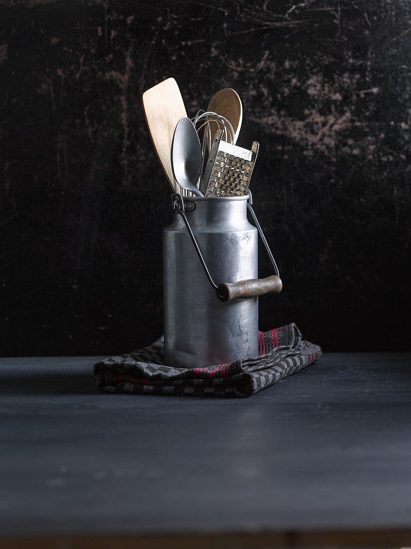 An old milk jug with a whisk, wooden spoon and grater