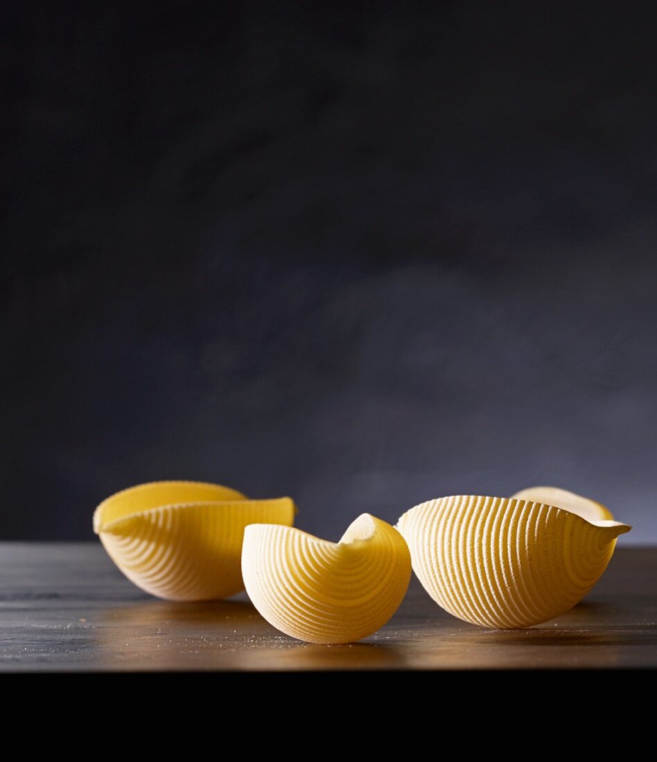 Three pieces of uncooked conchiglie pasta with a dark background