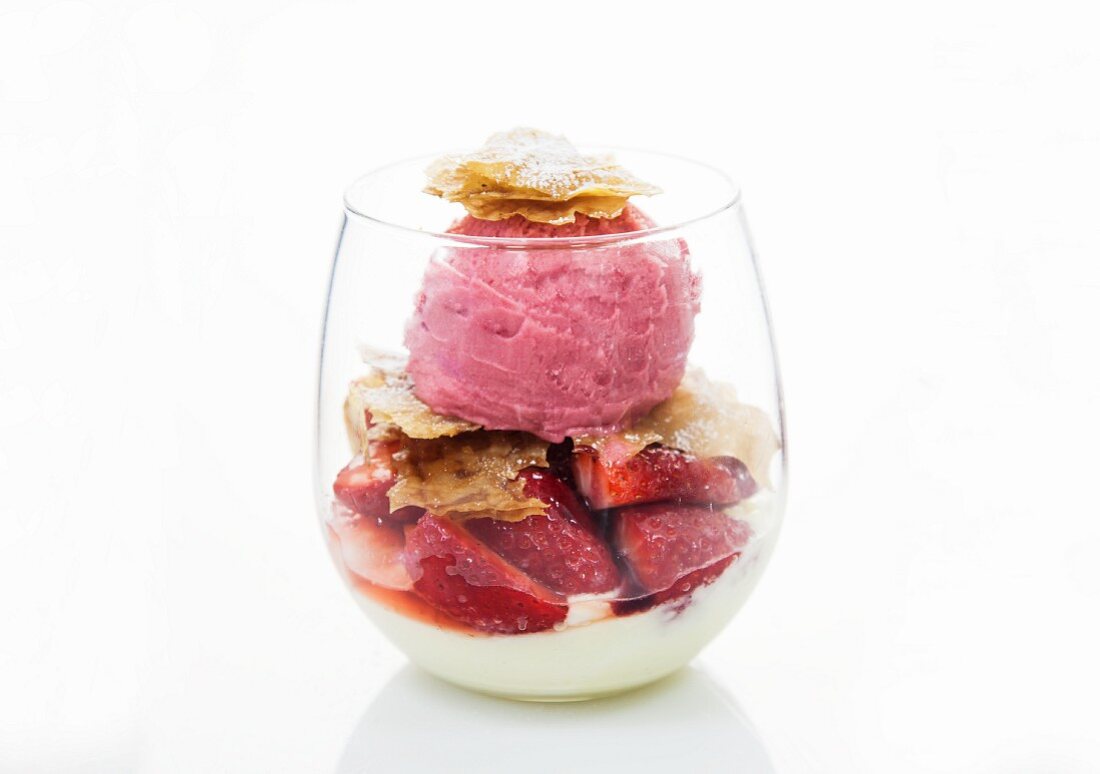 A strawberry ice cream sundae in a glass with flaky pastry