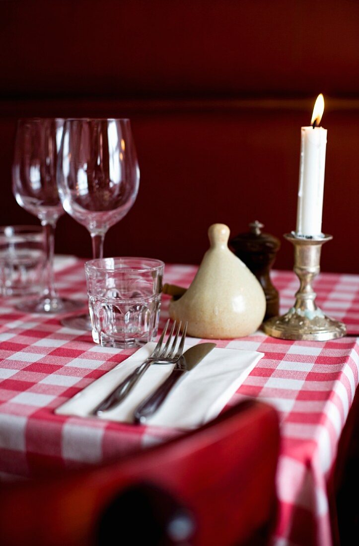 A dinner table set with a checked tablecloth, glasses and candlestick