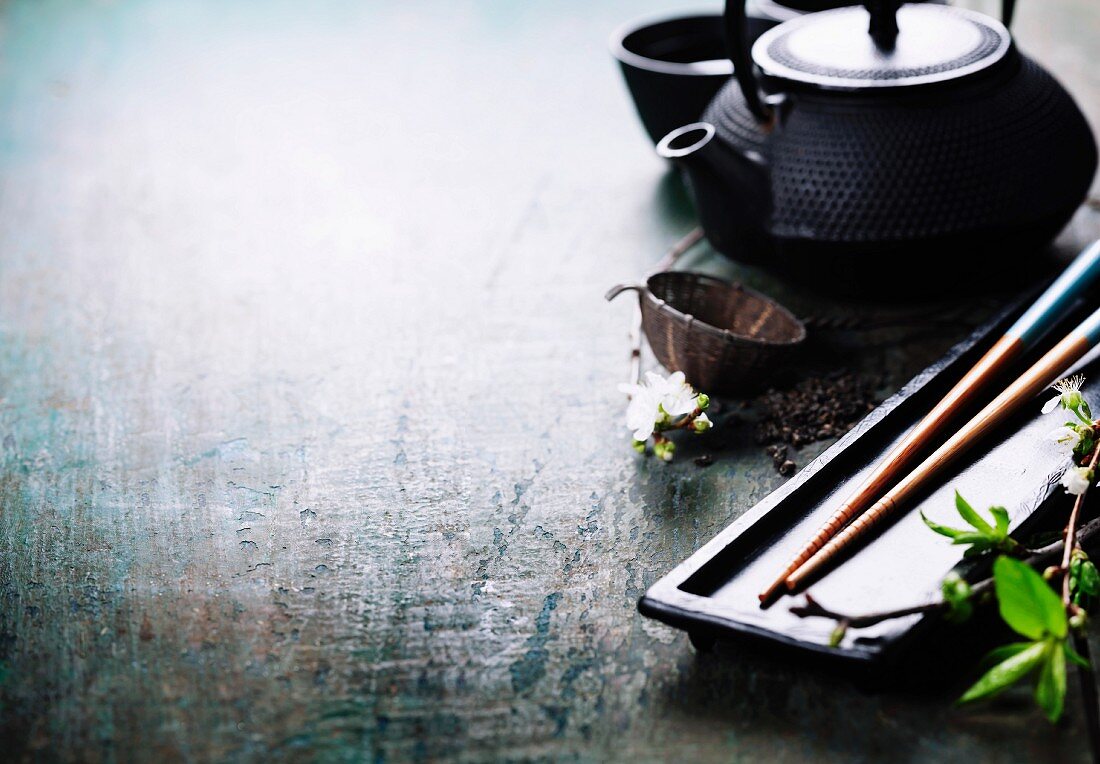 A Chinese tea set, chopsticks and a sakura branch on rustic wooden table