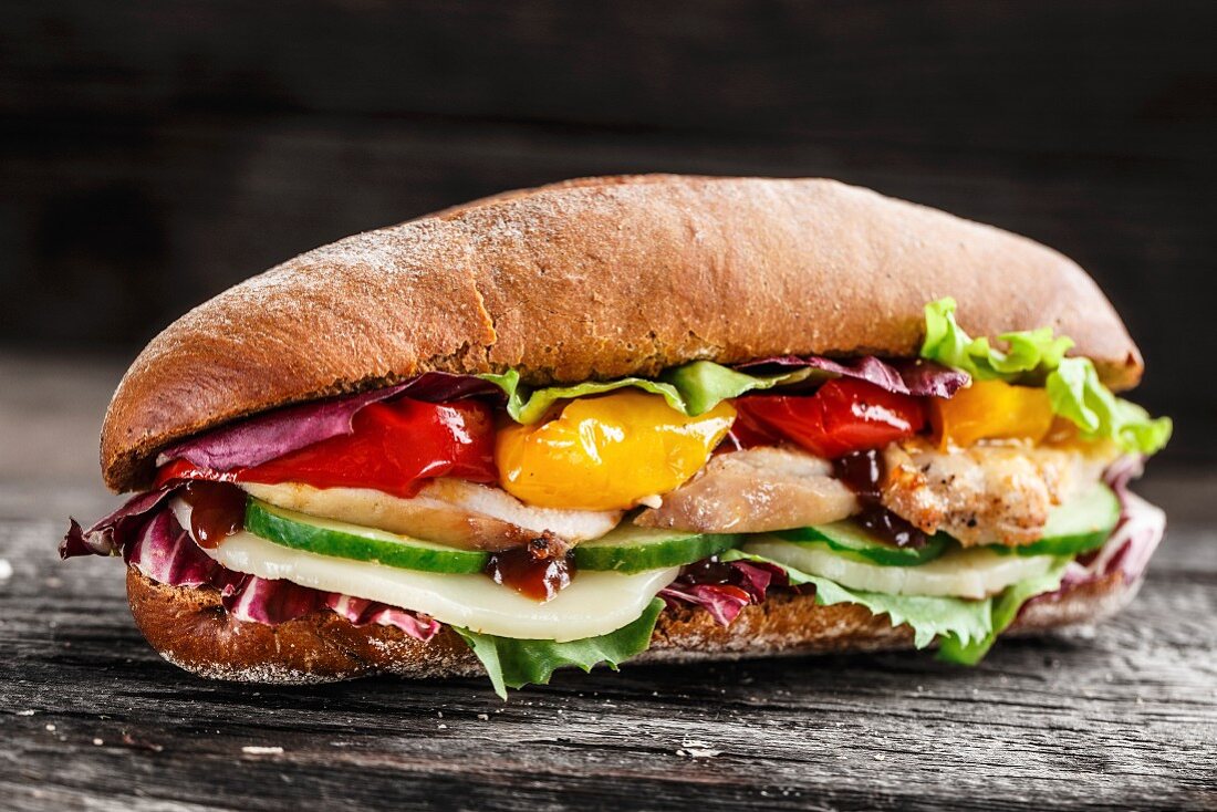 Sandwich mit Hähnchen, Käse und Gemüse auf rustikalem Holzuntergrund