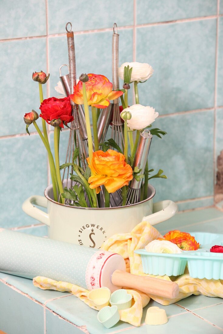Ranunculus and whisks arranged in old saucepan