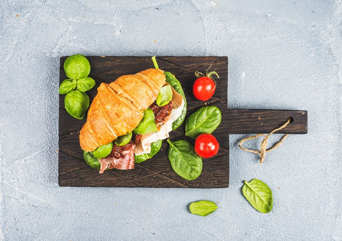Croissant-Sandwich mit Parmaschinken, getrockneten Tomaten, frischem Spinat und Basilikum