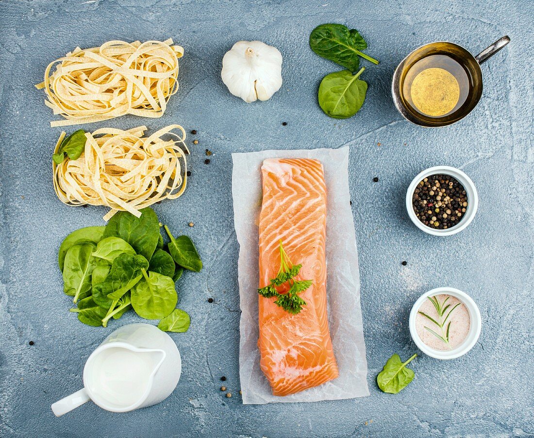 Zutaten für Nudelgericht: Tagliatelle, Lachs, Spinat und Sahne auf grauem Hintergrund