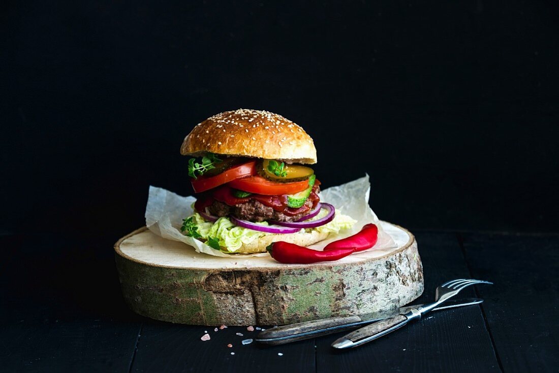 Fresh homemade burger on wooden serving board with red chili peppers over black background