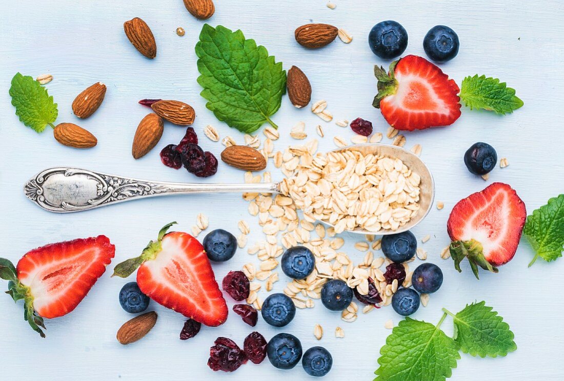 Zutaten für gesundes Frühstück: Haferflocken, Beeren, Mandeln und Minze auf blauem Untergrund