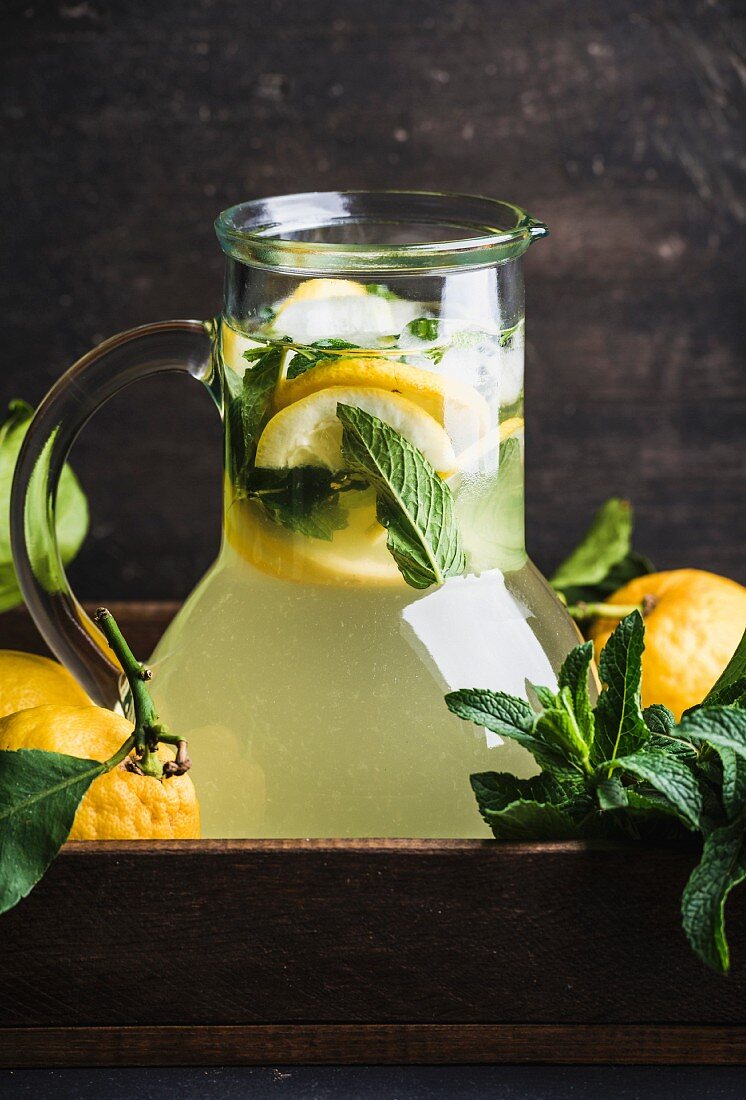 Homemade lemonade with mint and ice, served with fresh lemons in wooden tray